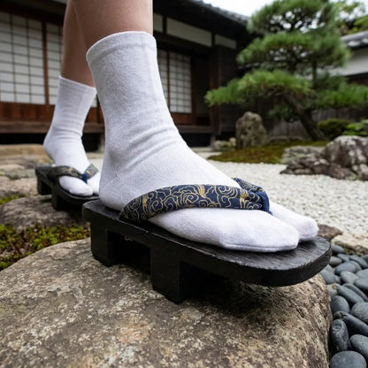 Geta Holzsandalen getragen mit weißen Tabi-Socken auf einem Stein im japanischen Garten