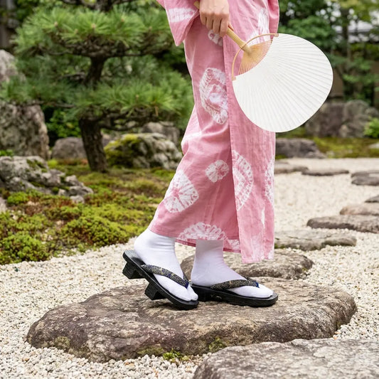Geta Holzsandalen getragen mit einem rosa Kimono im japanischen Garten