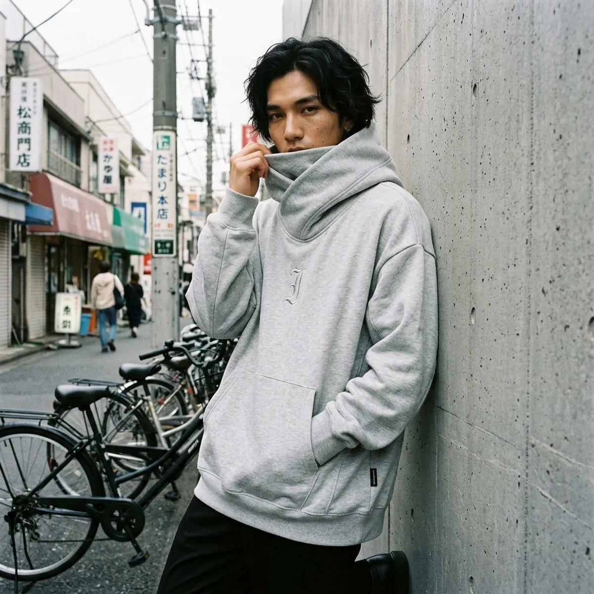 Oversized Hoodie mit hochgezogenem Trichterkragen über dem unteren Gesicht vor einer Betonwand