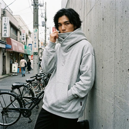 Oversized Hoodie mit hochgezogenem Trichterkragen über dem unteren Gesicht vor einer Betonwand