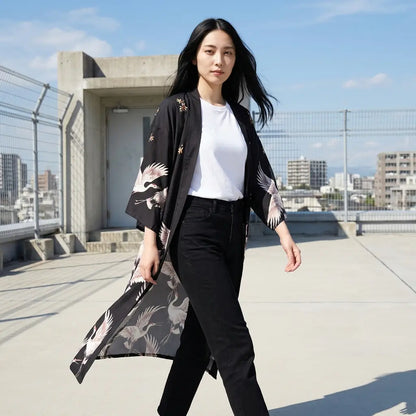 Langer schwarzer Kimono-Mantel für Damen mit grau-rosa Druckmuster, offen getragen auf einer Dachterrasse