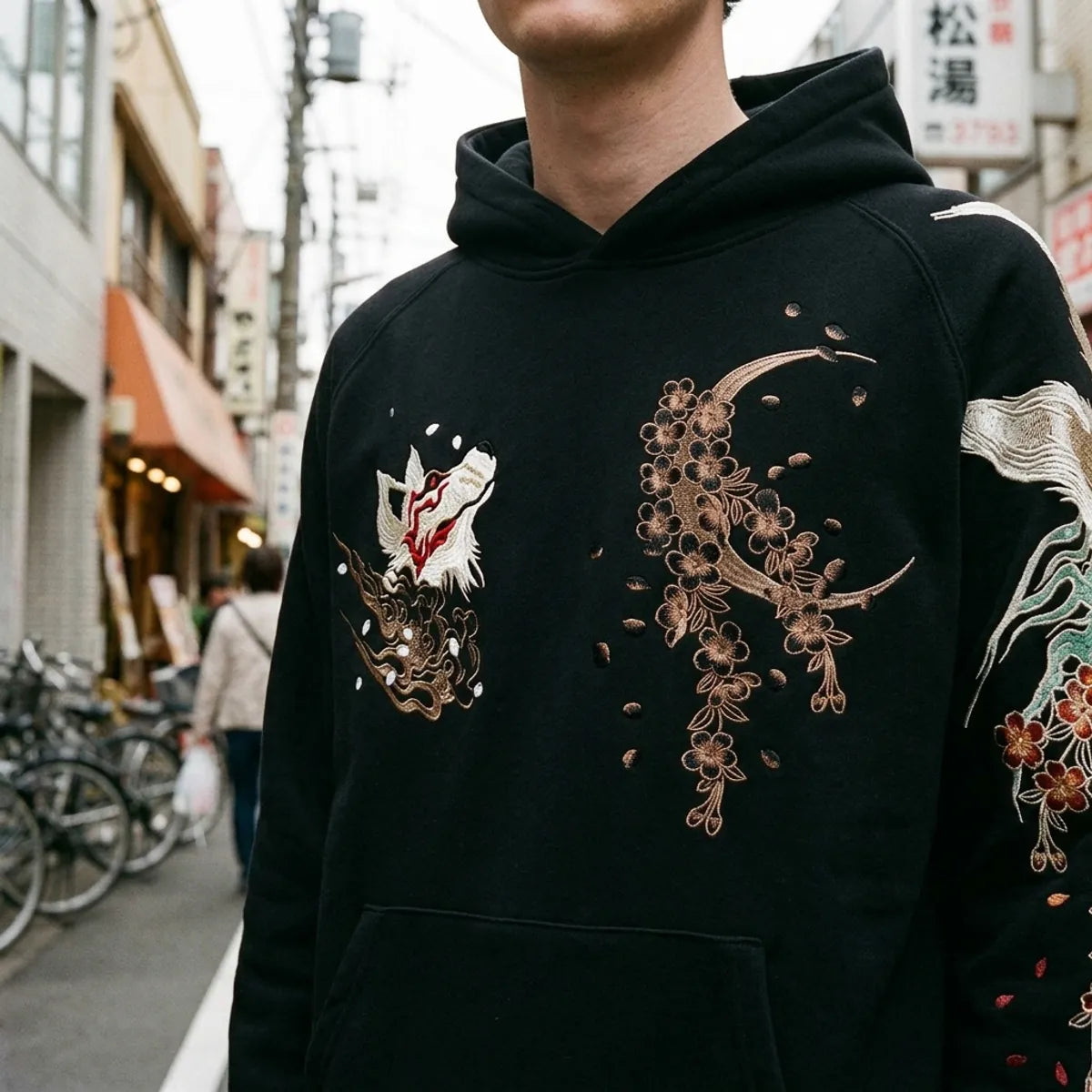 Nahaufnahme von bronzenem Halbmond und Kirschblüten auf der Brust des Hoodies bestickt