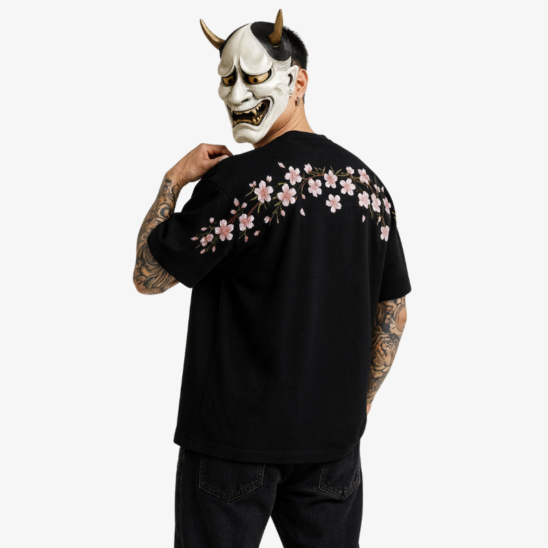 Mann trägt schwarzes Sakura Shirt und hält eine Hannya-Maske mit Hörnern