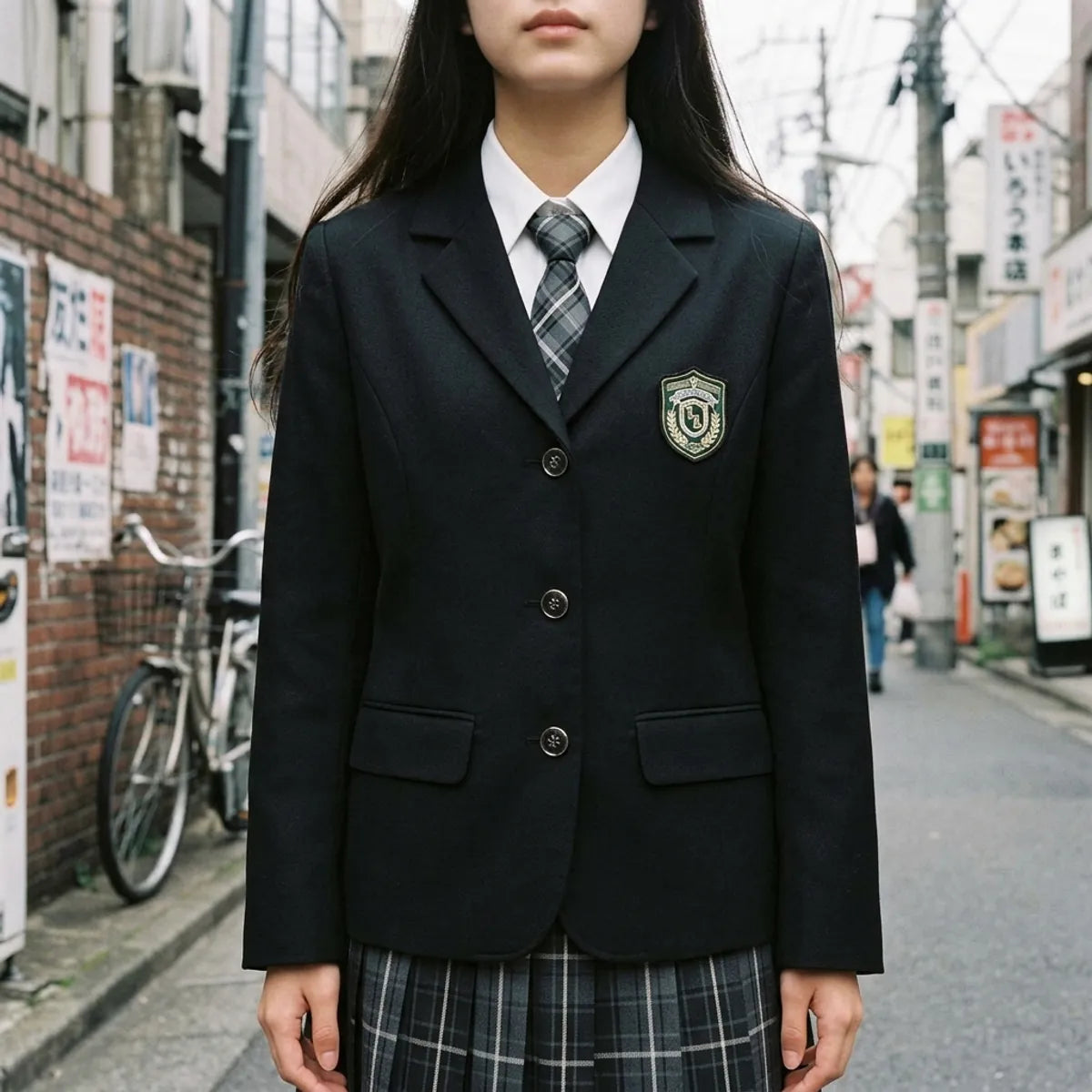 Nahaufnahme des schwarzen Schuluniform-Blazers mit gesticktem Wappen und karierter Krawatte